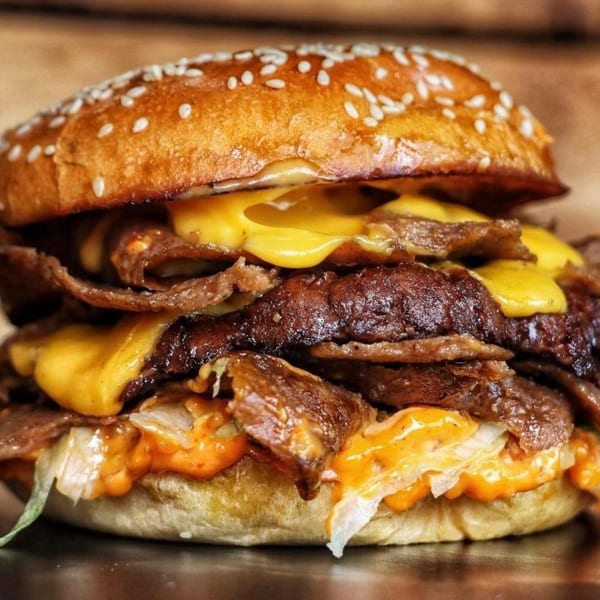 Large burger with multiple beef patties, melted cheese, lettuce, and special sauce on a sesame bun.